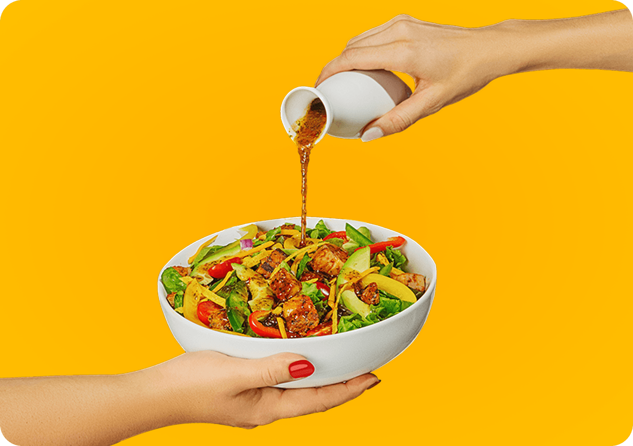 Chef pouring dressing over a fresh salad bowl